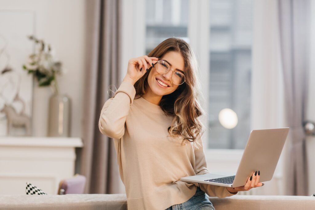 linda-chica-camisa-beige-tocando-gafas-sosteniendo-portatil-sonrisa