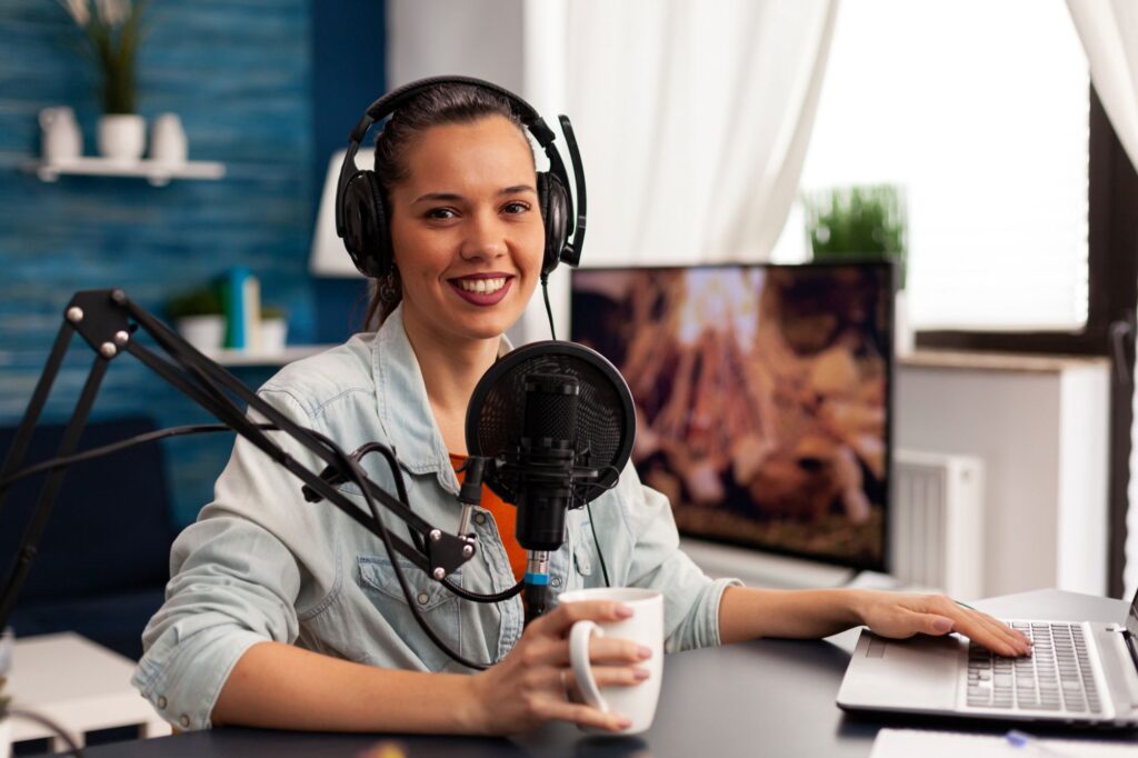 mujer-influyente-sonriente-sentada-frente-camara-grabando-video-blog-moda-blogger-digital-vlogger-streaming-talk-show-estudio-auriculares-microfono-podcast-profesional